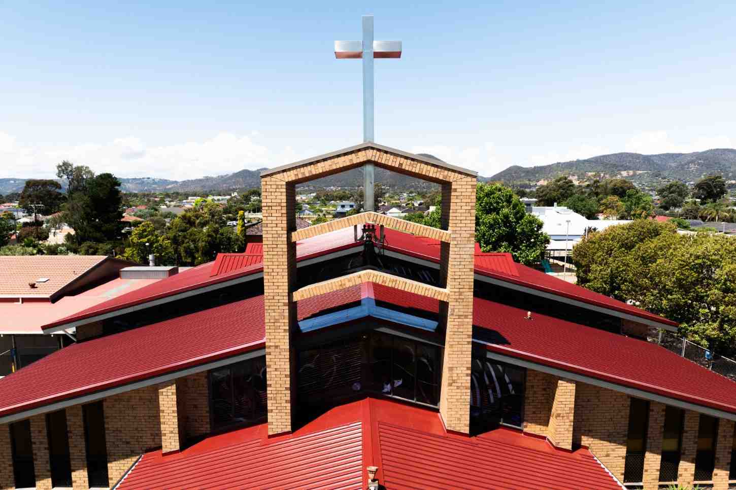 Church building with red metal roof and large cross on top overlooking a suburban area